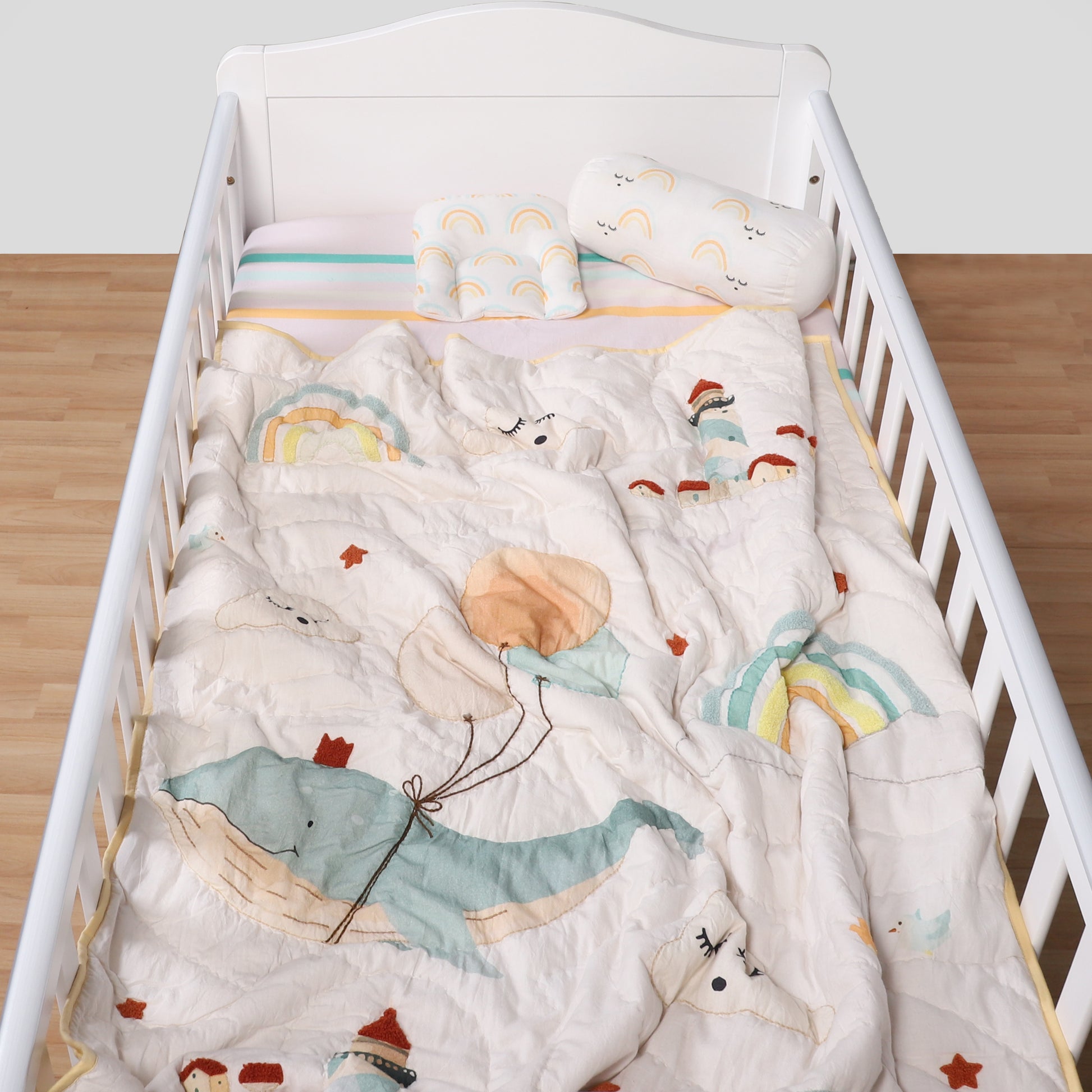 White crib with colorful bedding featuring cartoon animals and objects.