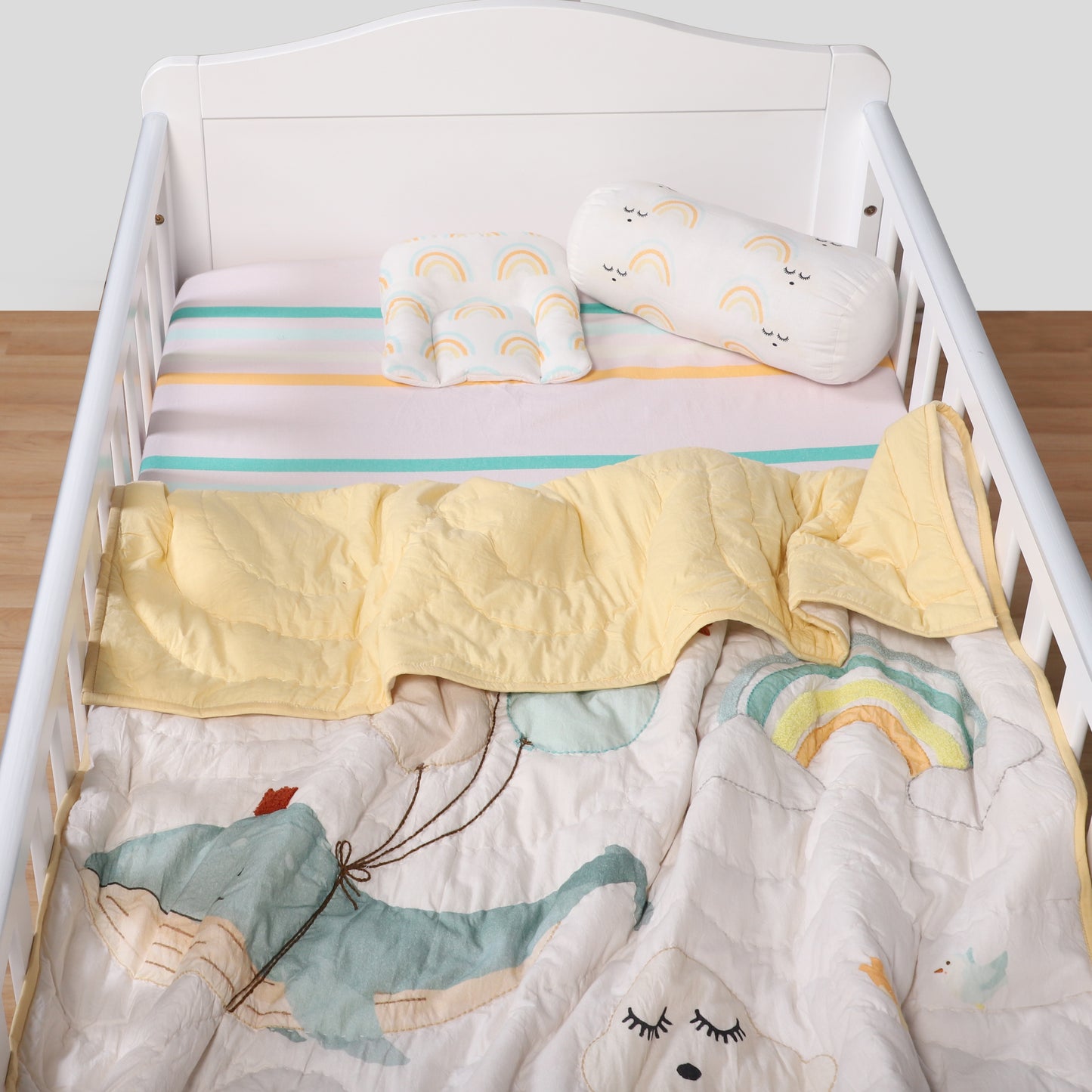 Children's crib with colorful bedding featuring cartoon animals and a rainbow.