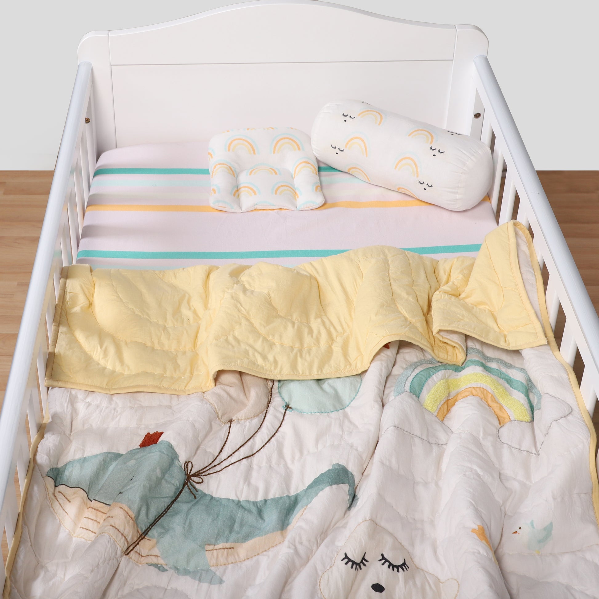 Children's crib with colorful bedding featuring cartoon animals and a rainbow.