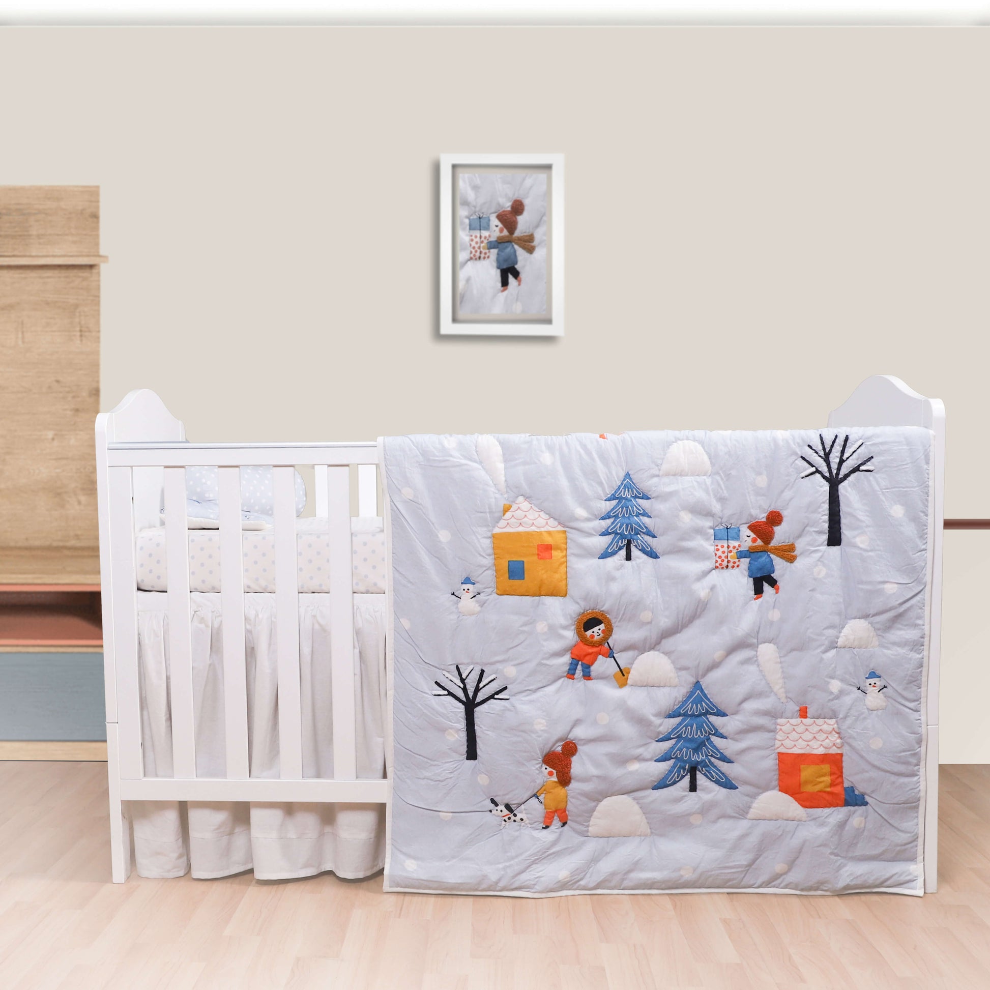 A baby quilt with a winter theme, featuring characters such as a snowman, trees, and possibly a bear, is displayed on a crib.
