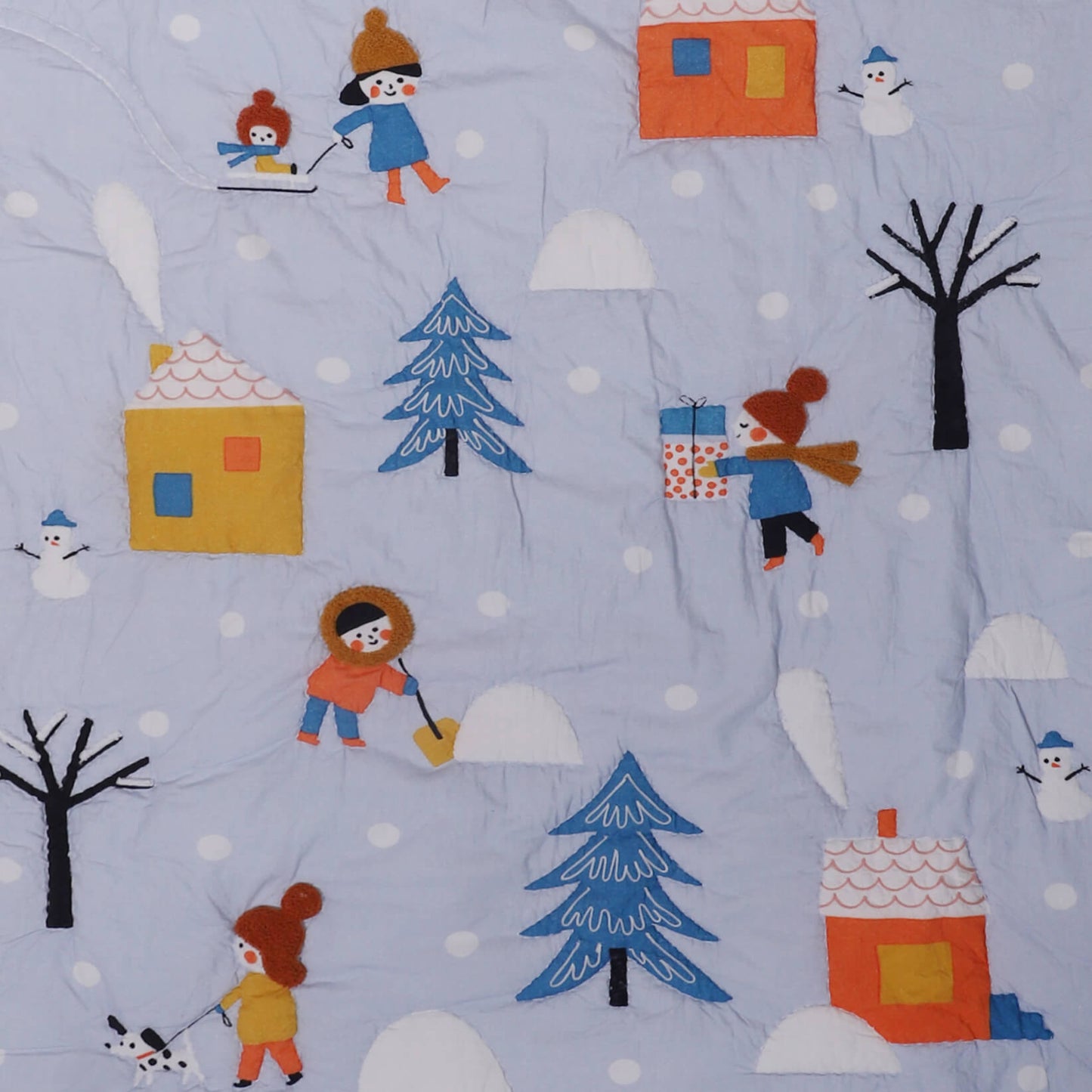 A baby quilt with a winter theme, featuring characters such as a snowman, trees, and possibly a bear, is displayed on a crib.