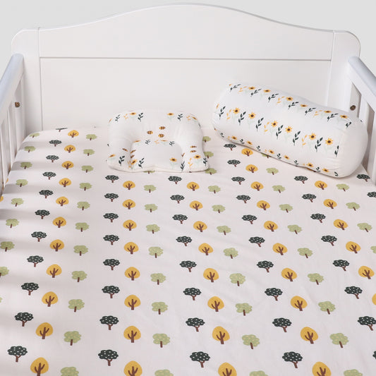 Crib with tree-patterned bedding and matching pillows on a white background
