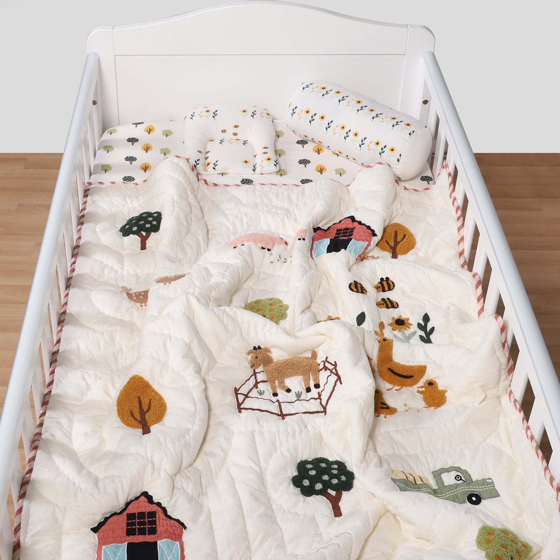 Crib with white bedding featuring animal and nature patterns on a wooden floor.