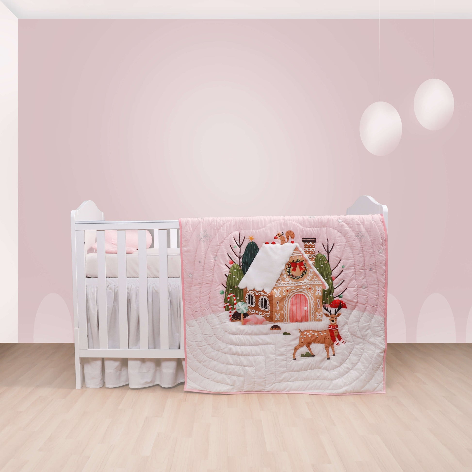 A baby quilt with a Christmas theme displayed on a crib, featuring a cottage and a reindeer.