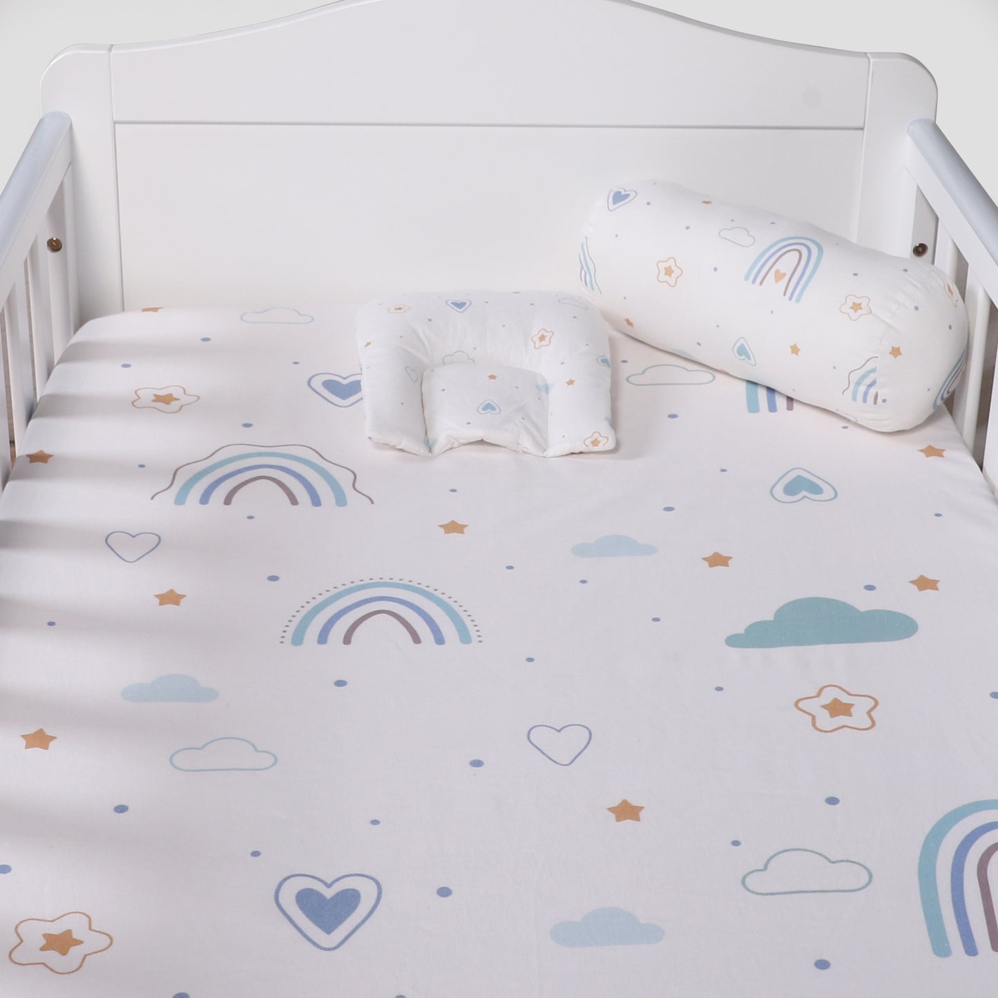 Crib with rainbow, cloud, and heart patterned bedding and pillows.