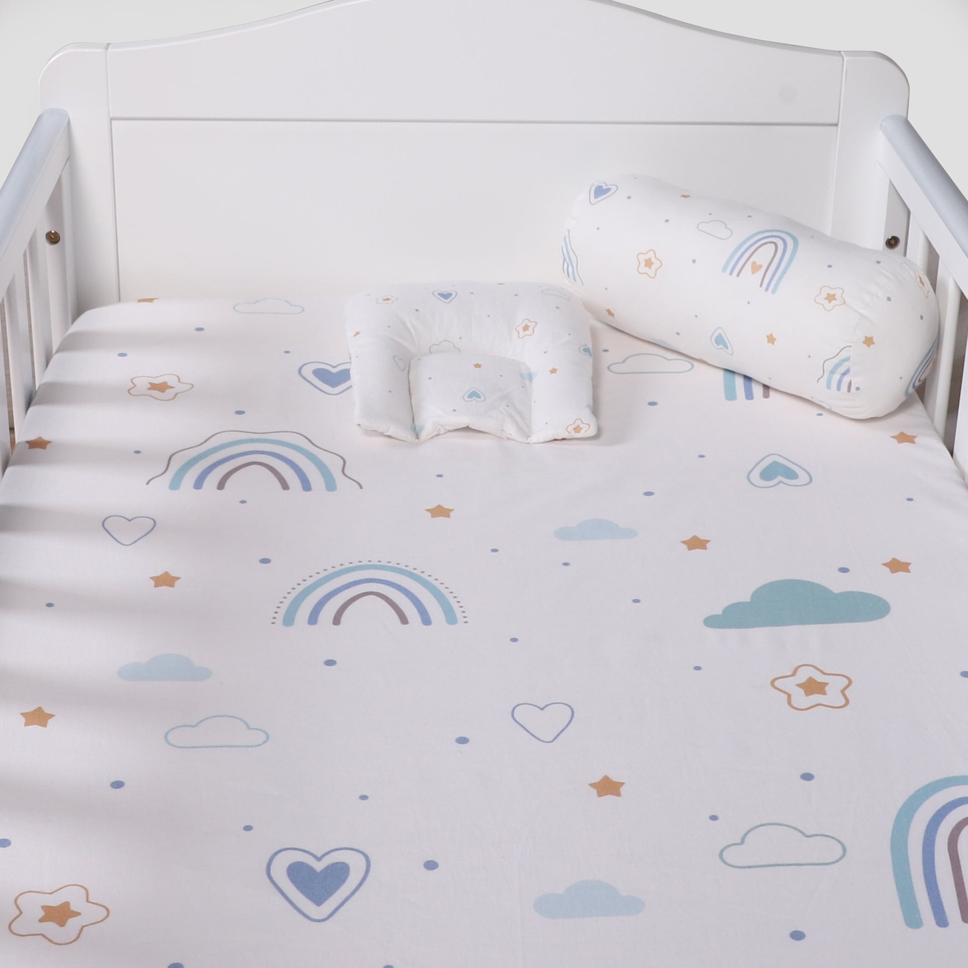 Crib with rainbow, cloud, and heart patterned bedding and pillows.