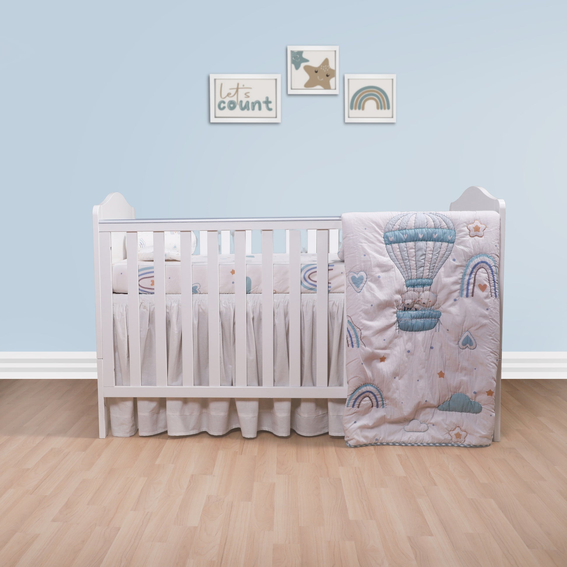 Baby crib with decorative bedding featuring hot air balloons and rainbows in a nursery setting.
