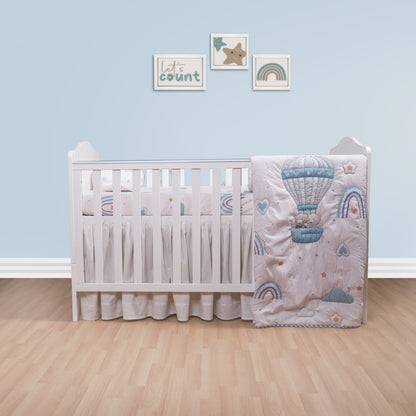 Baby crib with decorative bedding featuring hot air balloons and rainbows in a nursery setting.