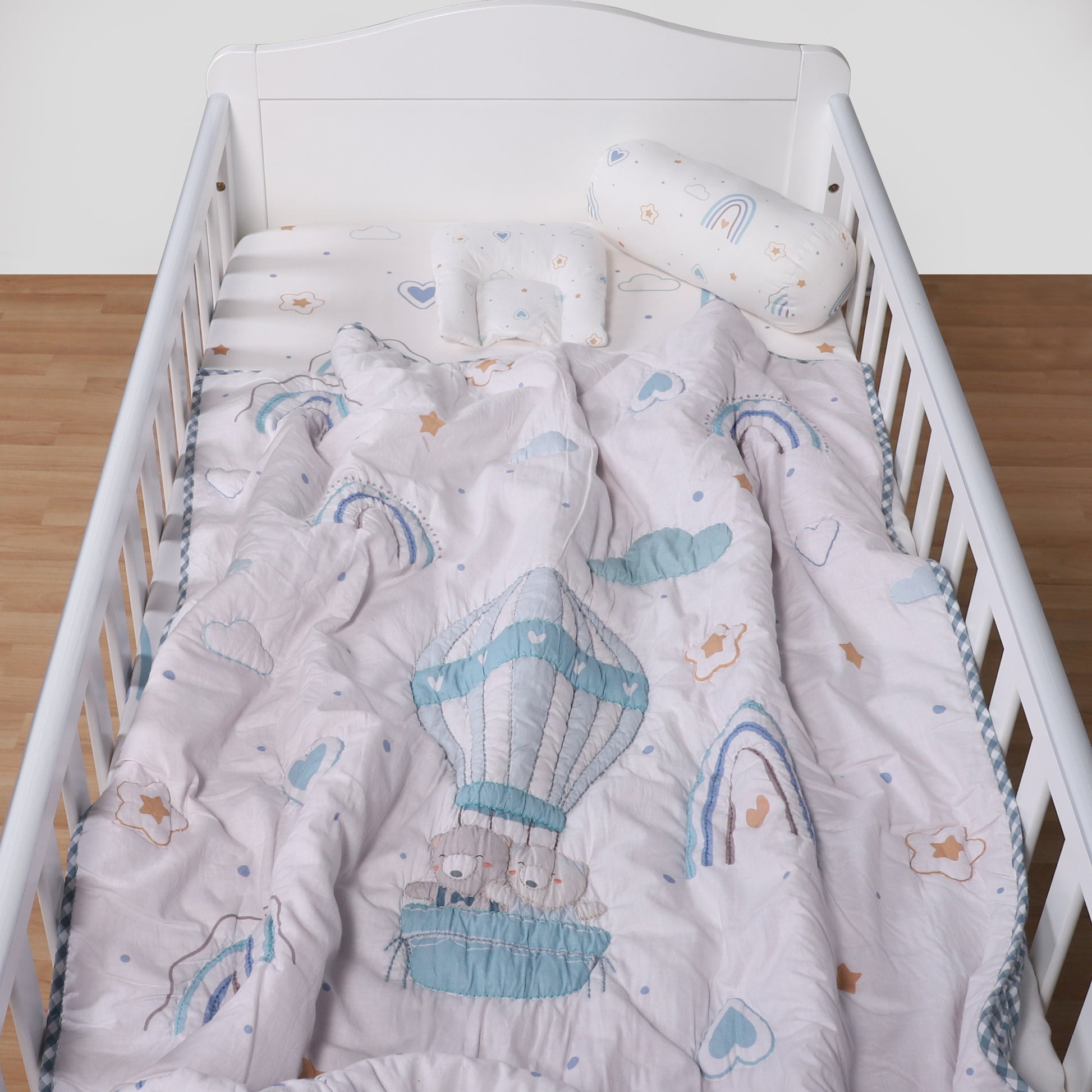 Baby crib with a gray comforter featuring hot air balloons and rainbows on a white background.