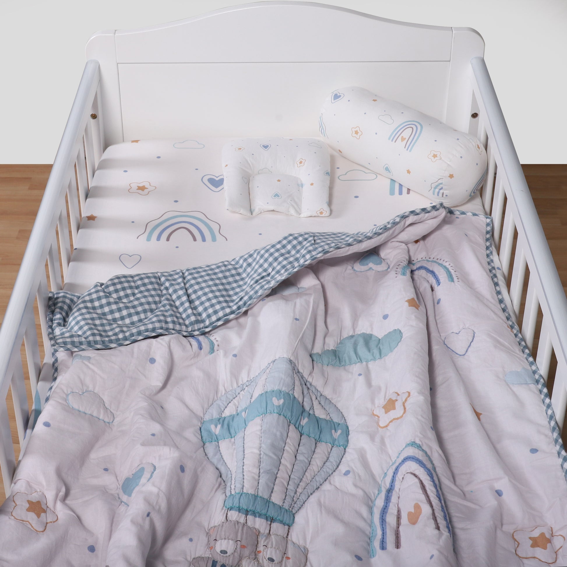 White crib with baby bedding featuring clouds, stars, and rainbow patterns.
