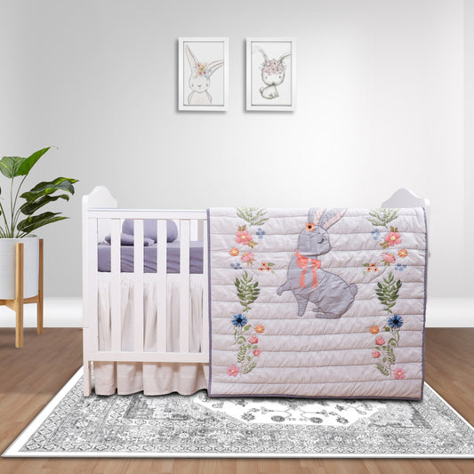Crib with decorative quilt featuring a rabbit and floral design in a room with a plant and wall art.