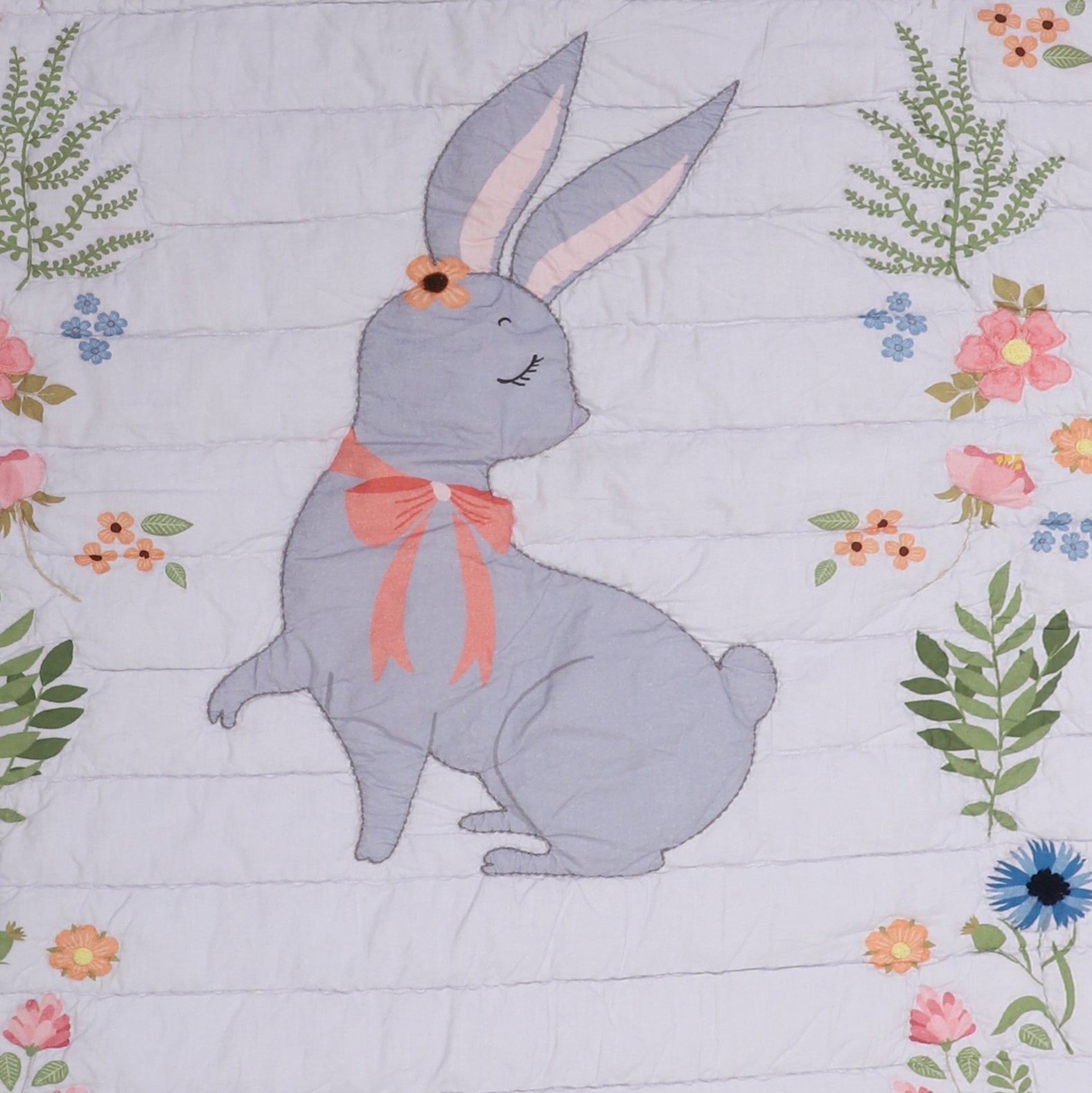 Quilt with a gray bunny wearing a pink bow surrounded by flowers and leaves on a light purple background
