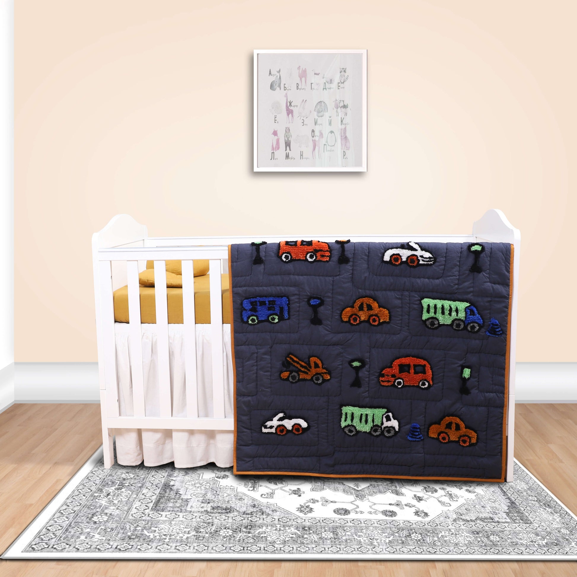 A baby quilt with a black background featuring colorful embroidered vehicles around the border, displayed on a white crib.
