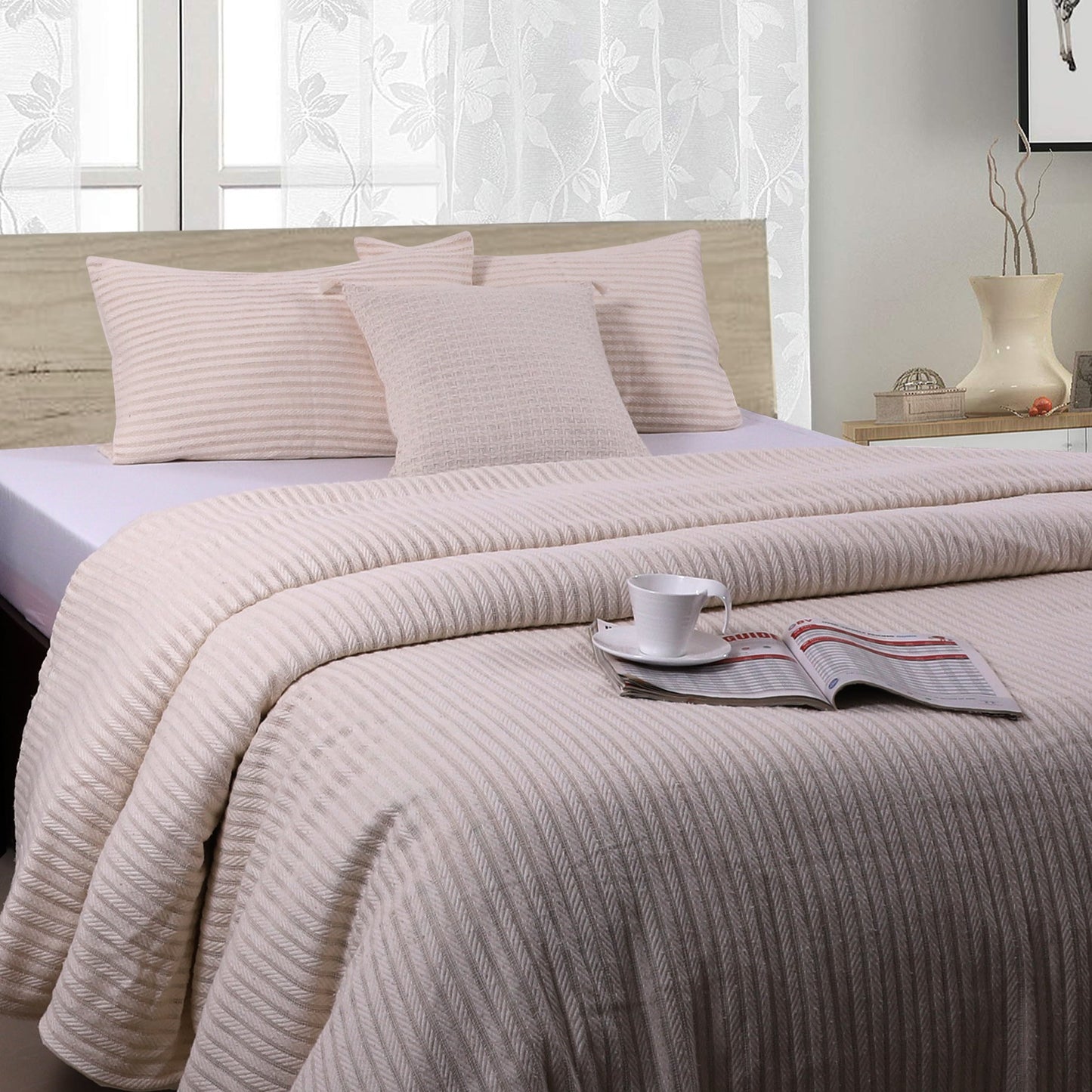 A beige duvet cover with a striped pattern, displayed on a bed in a bedroom setting. The cover appears to be neatly made, with pillows and a cup of coffee placed on the bed.