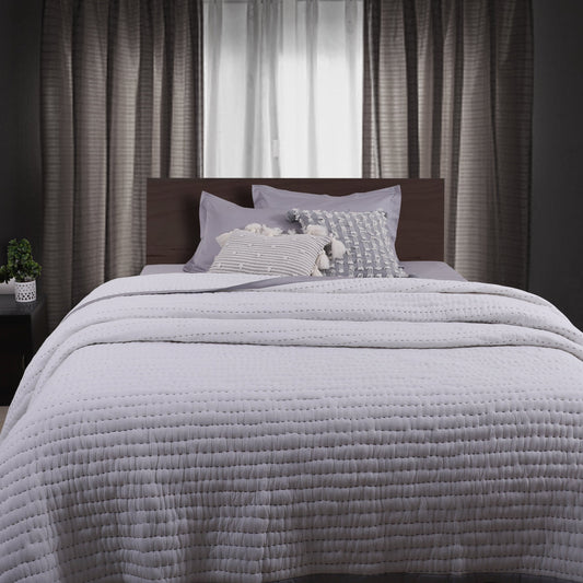 A neatly made bed with a white, solid color quilt and pillows, with curtains in the background.