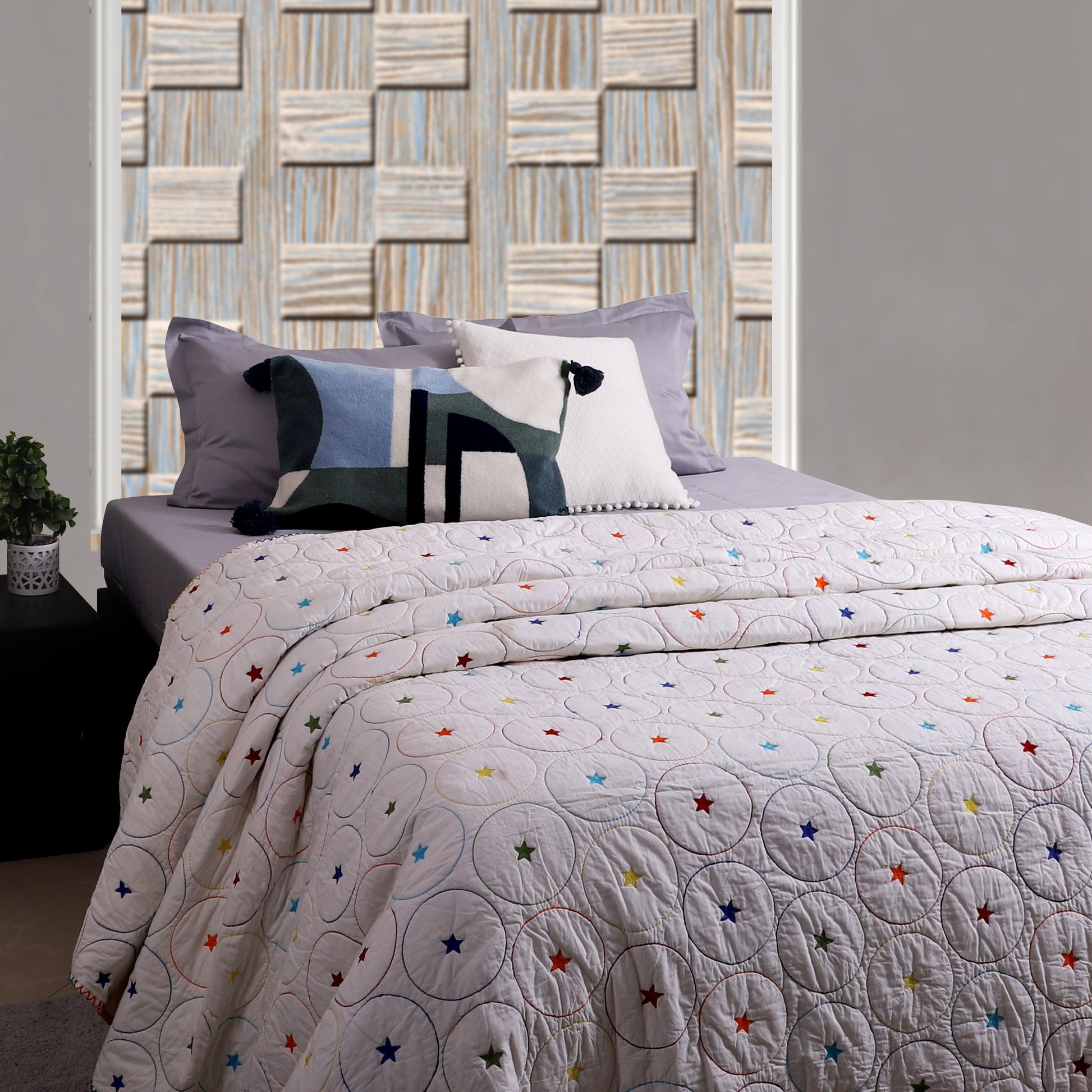 A multicolored quilt with a geometric pattern displayed on a bed in a room with a decorative wall panel.