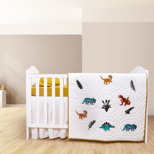 A colorful baby quilt with dinosaur patterns displayed on a crib.