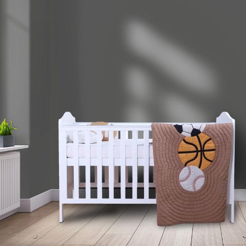 A baby quilt with sports balls design placed on a white crib, with a gray wall in the background and a small plant to the side.