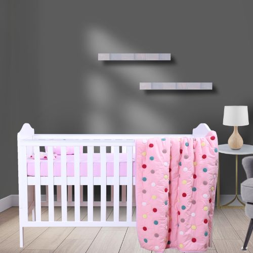 A baby quilt with a pink background and multicolored polka dots, displayed on a white crib with bedding set coordination.