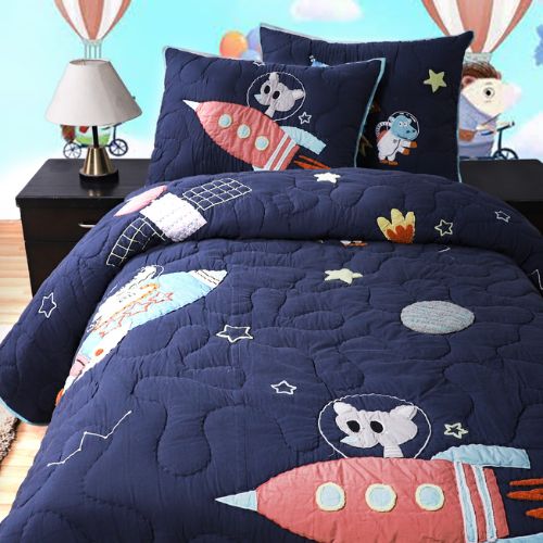 A kids' quilt set with a space theme, including rockets and planets, on a navy background displayed on a bed with matching pillowcases.