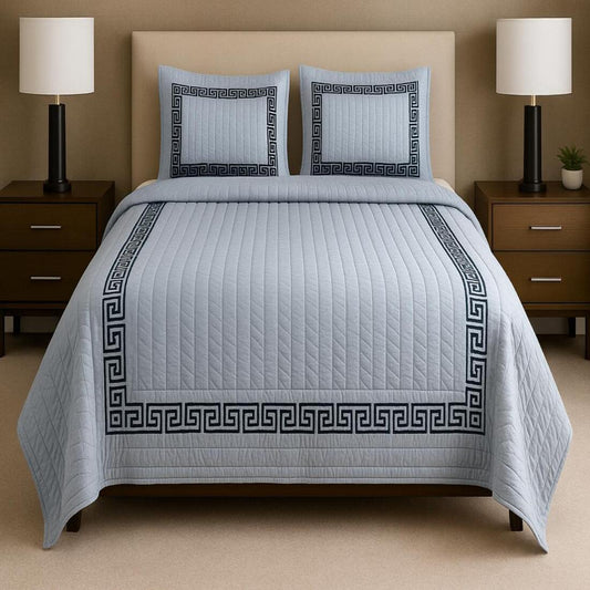 Bed with gray quilt and pillowcases in a bedroom setting with lamps and nightstands.