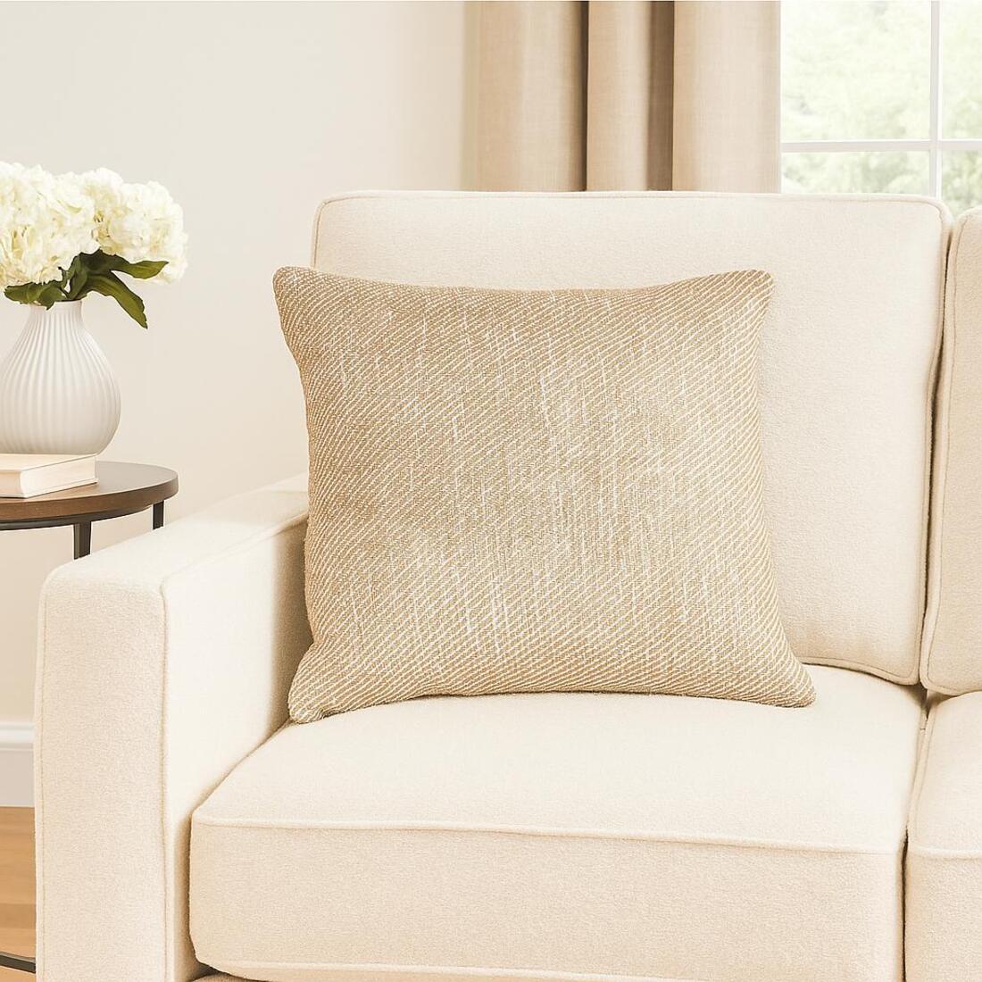 Beige pillow on a beige sofa with a side table and flowers in the background