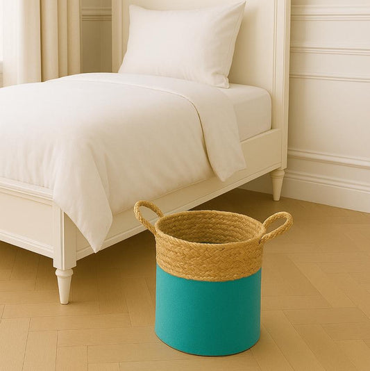 Woven basket with teal bottom and beige top on a wooden floor next to a bed.