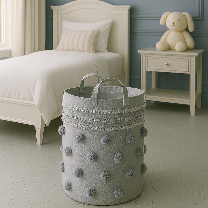 Gray laundry basket with pom-poms in a bedroom setting