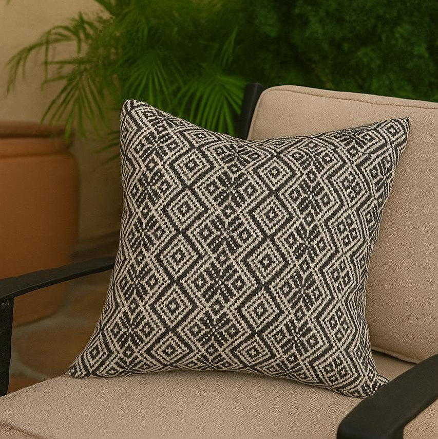 Decorative pillow with geometric pattern on a beige chair outdoors.