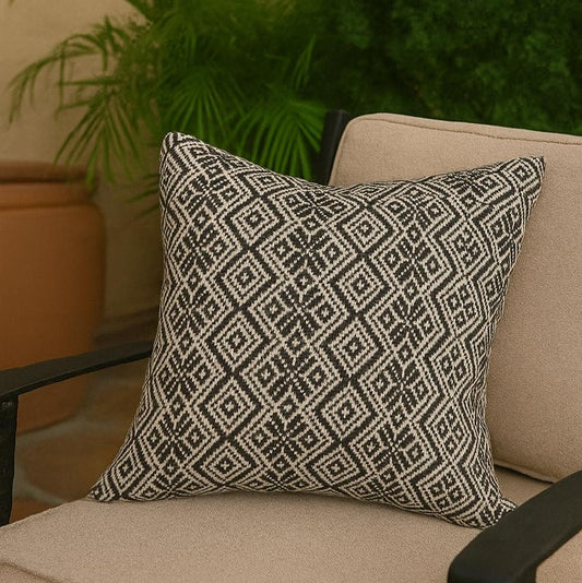 Decorative pillow with geometric pattern on a beige chair outdoors.