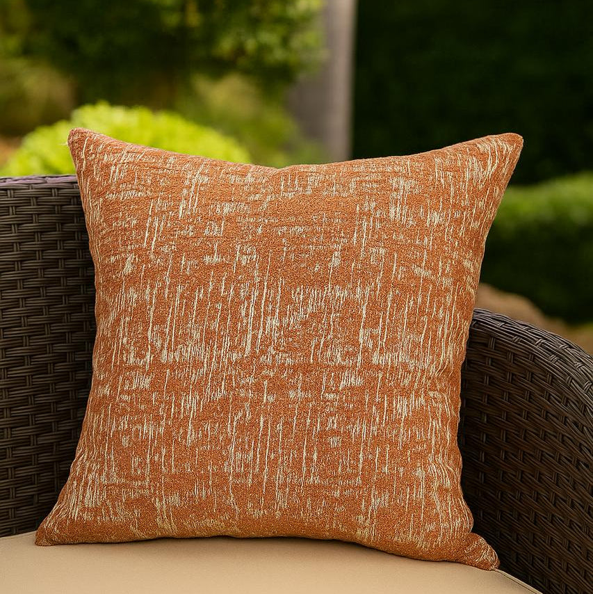Textured orange pillow on a wicker chair with a blurred green outdoor background