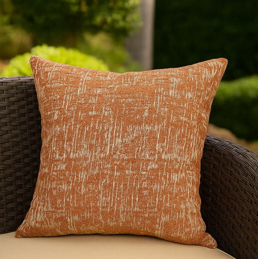 Textured orange pillow on a wicker chair with a blurred green outdoor background