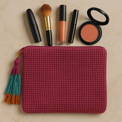 Pink textured makeup pouch with cosmetic items on a beige background