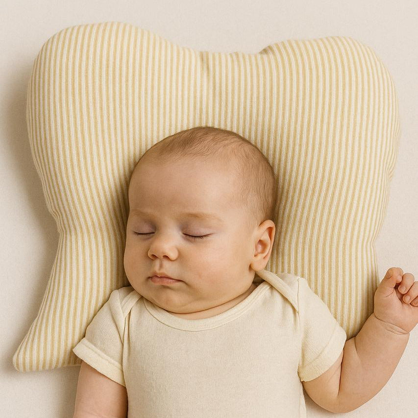 Baby in a white onesie lying on a striped pillow against a beige background