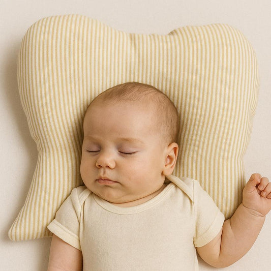 Baby in a white onesie lying on a striped pillow against a beige background