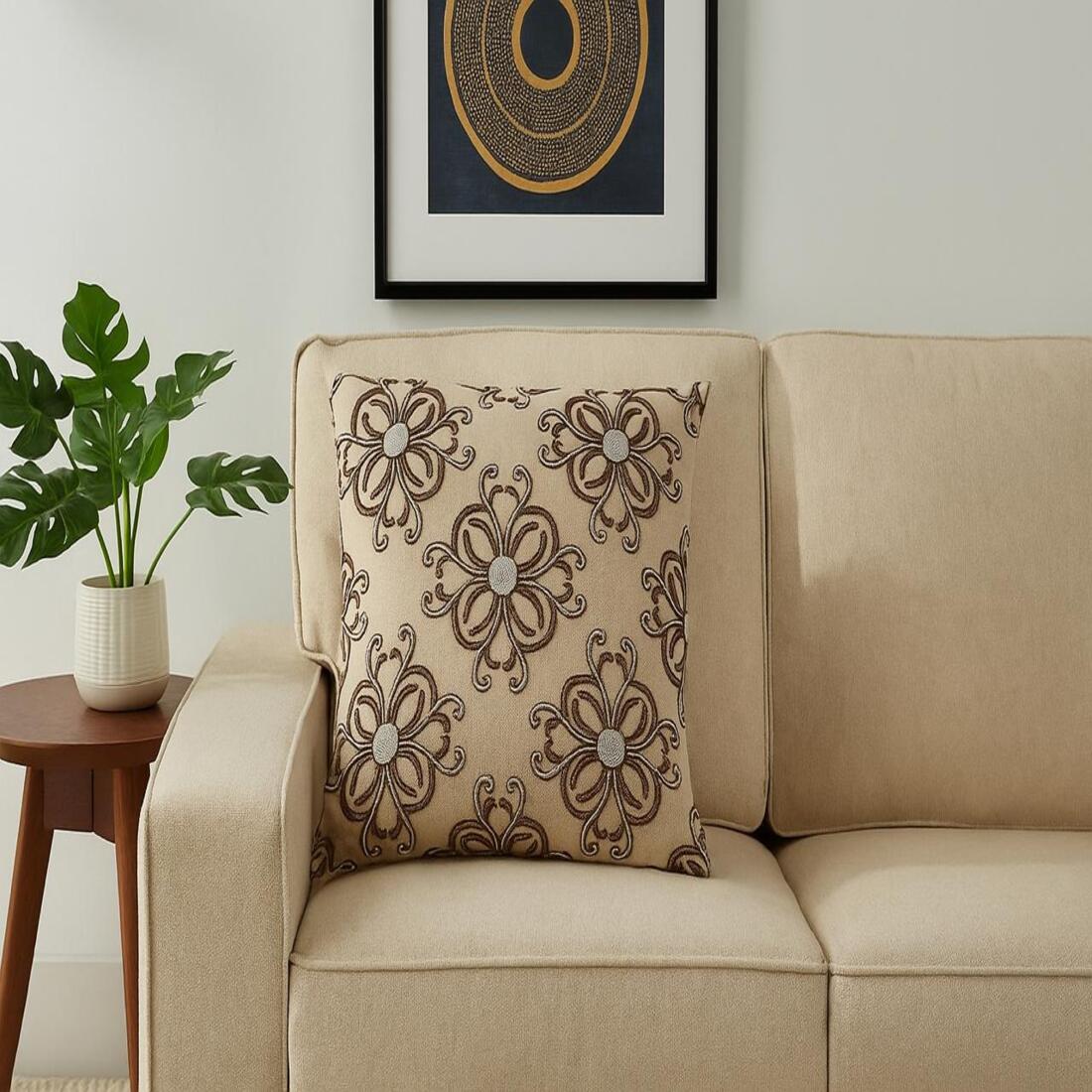 Decorative pillow on a beige sofa with a plant and framed art in the background