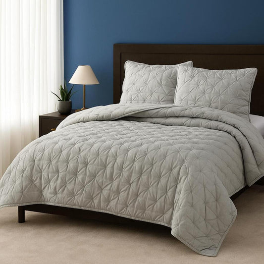 Gray quilted comforter set on a bed with a dark wooden headboard against a blue wall.