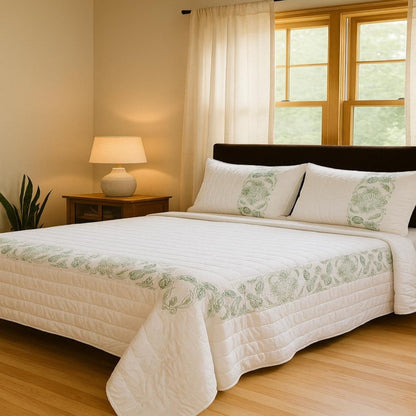 Bedroom with a bed covered in white bedding with green patterns, a lamp on a nightstand, and a window with curtains.