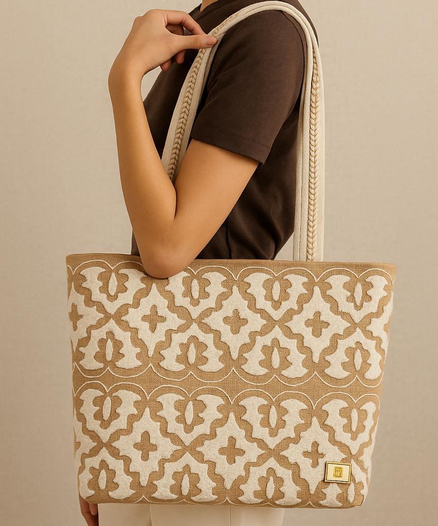 Person holding a beige tote bag with a white geometric pattern against a beige background