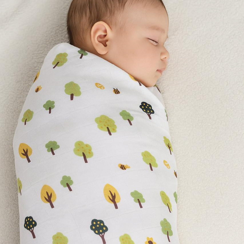 Baby swaddled in a blanket with tree pattern on a neutral background