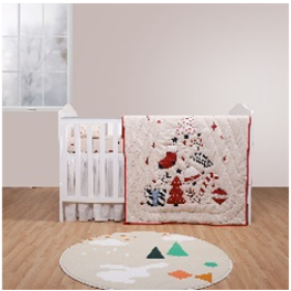 A baby quilt with Christmas motifs displayed on a crib, with a round baby pillow featuring similar design on the floor.